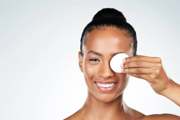 Roześmiana, piękna ciemnoskóra kobieta przykłada do jednego oka wacik kosmetyczny